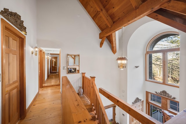 hall with wooden ceiling, high vaulted ceiling, an inviting chandelier, light wood-type flooring, and beam ceiling