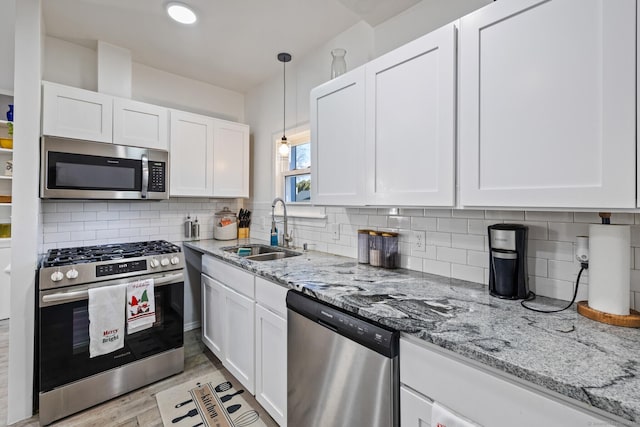 kitchen with sink, stainless steel appliances, pendant lighting, white cabinets, and light wood-type flooring