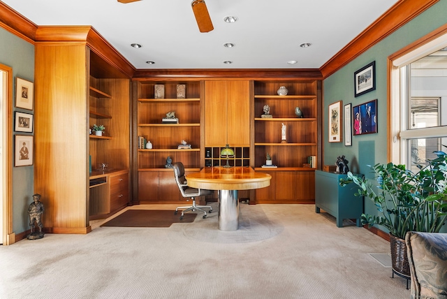 carpeted office featuring built in shelves, crown molding, ceiling fan, and built in desk