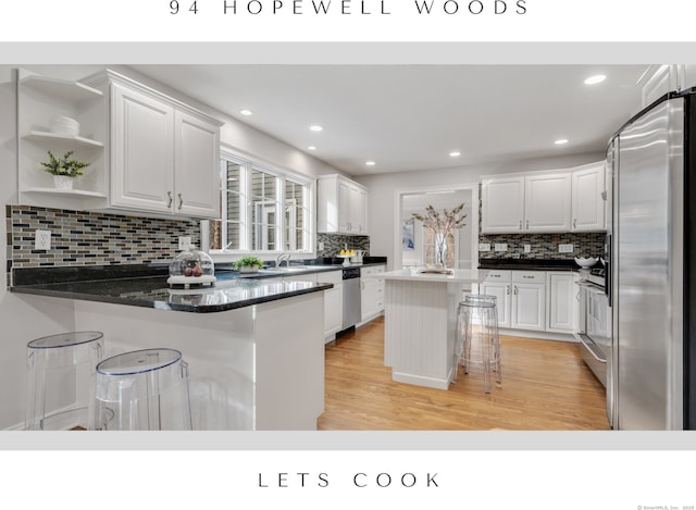 kitchen featuring white cabinetry, light hardwood / wood-style floors, kitchen peninsula, a breakfast bar area, and stainless steel appliances