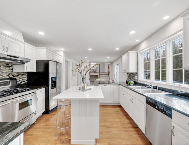 kitchen featuring a kitchen bar, appliances with stainless steel finishes, ventilation hood, sink, and white cabinetry