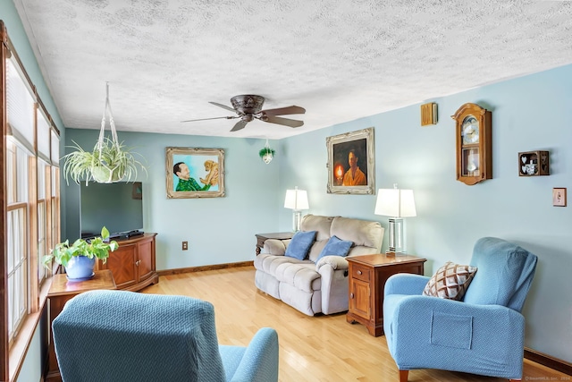 living room featuring ceiling fan, light hardwood / wood-style flooring, and a textured ceiling