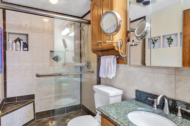 bathroom with an enclosed shower, vanity, a textured ceiling, tile walls, and toilet