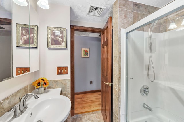 bathroom featuring shower / bath combination with glass door, a textured ceiling, tile walls, and sink