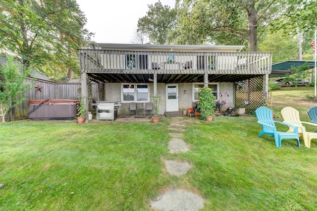 rear view of house with a hot tub, a lawn, and a wooden deck