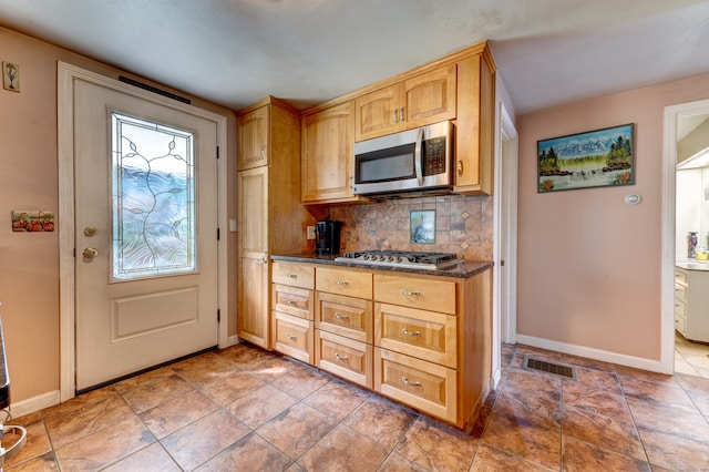 kitchen with light brown cabinets, dark stone countertops, decorative backsplash, light tile patterned floors, and appliances with stainless steel finishes