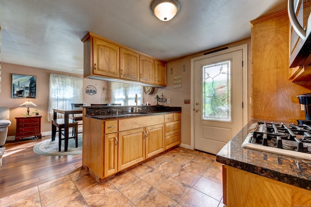 kitchen featuring kitchen peninsula, appliances with stainless steel finishes, dark stone counters, sink, and light hardwood / wood-style floors