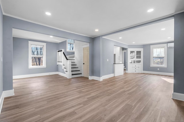 unfurnished living room featuring light hardwood / wood-style floors, crown molding, and a wall unit AC