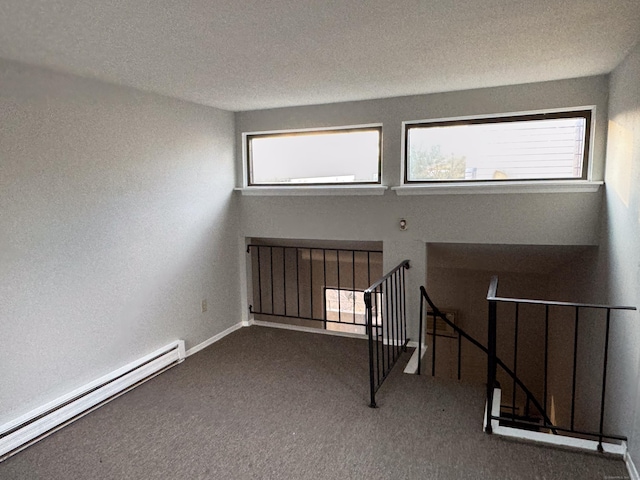 carpeted spare room featuring a textured ceiling, plenty of natural light, and baseboard heating