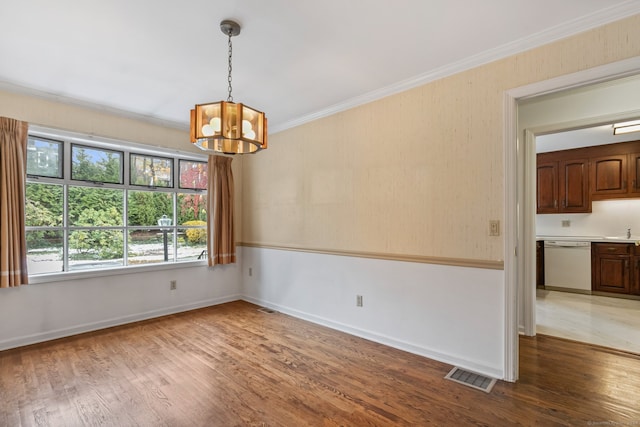 unfurnished dining area with sink, ornamental molding, wood-type flooring, and a notable chandelier