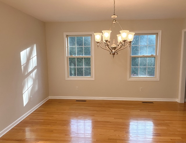 spare room with a chandelier and light wood-type flooring