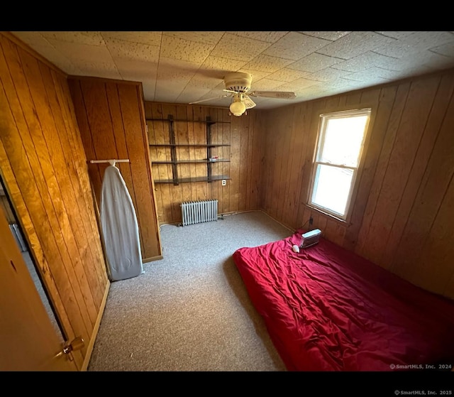 carpeted bedroom featuring radiator heating unit and wooden walls