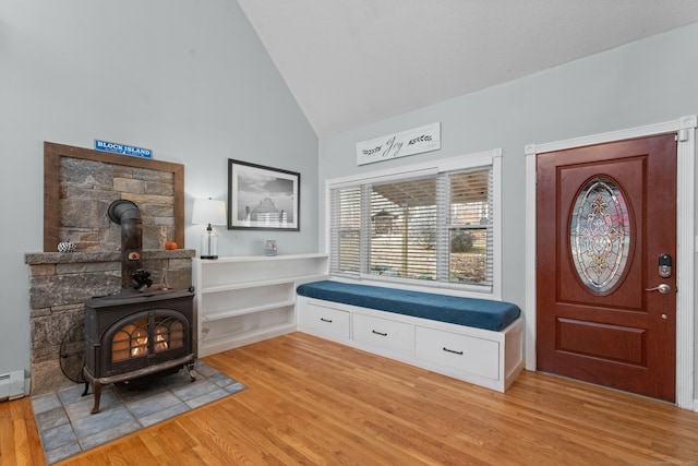 sitting room featuring light wood-type flooring, high vaulted ceiling, a wood stove, and baseboard heating