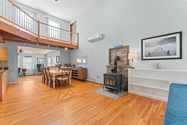 dining area with light hardwood / wood-style floors, a wall unit AC, a wood stove, and a wealth of natural light