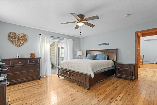 bedroom featuring a wall mounted AC, ceiling fan, light hardwood / wood-style floors, and a textured ceiling