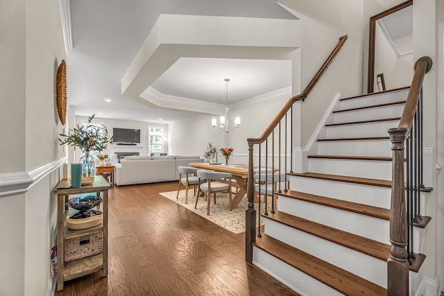 stairway with a raised ceiling, crown molding, hardwood / wood-style floors, and a notable chandelier