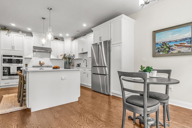 kitchen featuring appliances with stainless steel finishes, white cabinetry, hanging light fixtures, and wood-type flooring