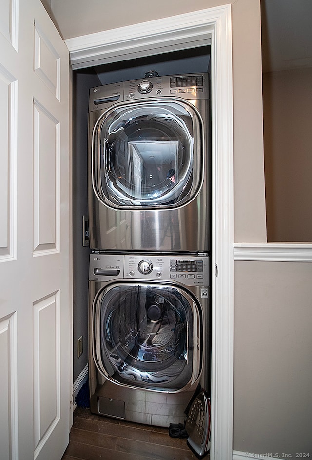 clothes washing area with dark wood-type flooring and stacked washer and clothes dryer