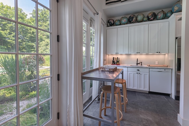 kitchen with tasteful backsplash, white cabinetry, sink, and white dishwasher