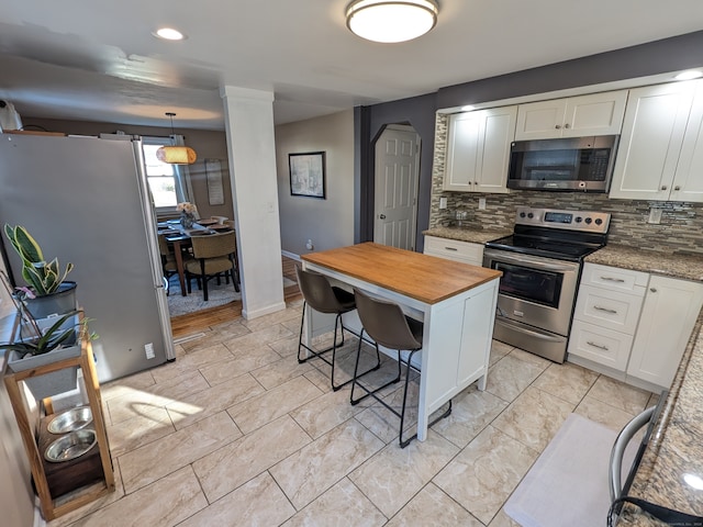 kitchen featuring light stone countertops, stainless steel appliances, decorative light fixtures, white cabinetry, and a breakfast bar area