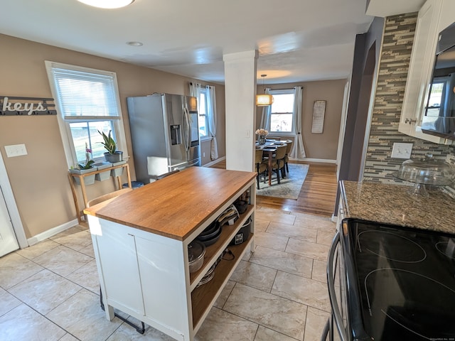 kitchen with white cabinetry, stainless steel fridge with ice dispenser, black range oven, and a healthy amount of sunlight