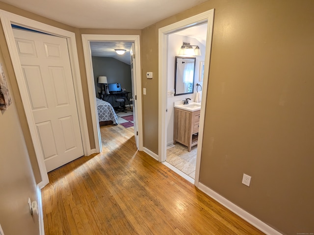 hallway with sink, light hardwood / wood-style floors, and lofted ceiling