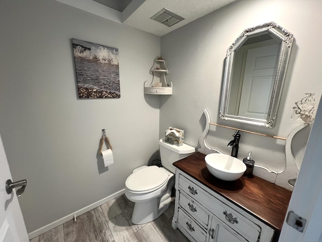 bathroom featuring vanity, toilet, wood finished floors, a textured ceiling, and baseboards