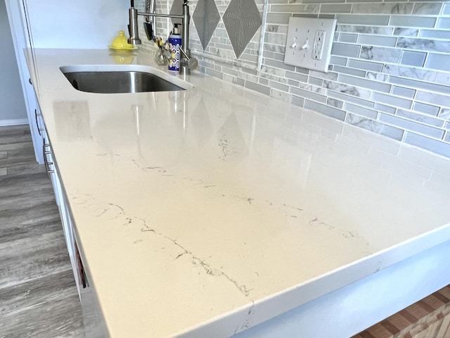 kitchen view of a sink, decorative backsplash, light stone counters, and wood finished floors