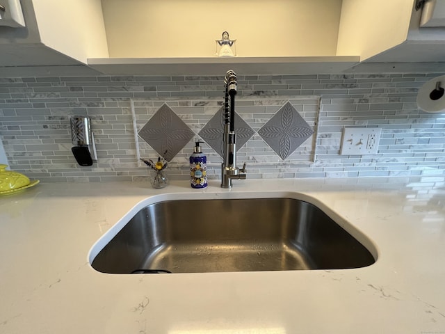 kitchen view of a sink, decorative backsplash, and light stone counters