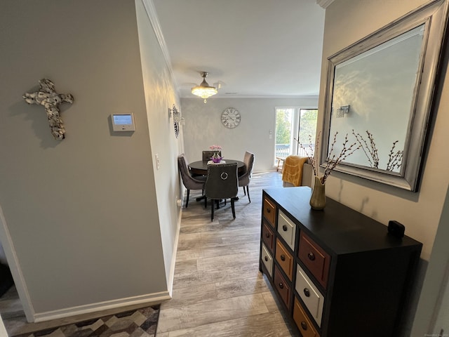 corridor featuring crown molding, light wood-style flooring, and baseboards