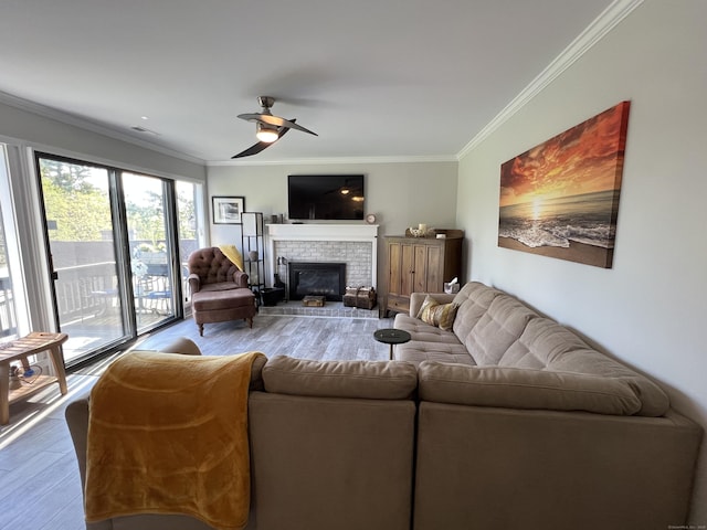 living room featuring wood finished floors, ceiling fan, crown molding, and a brick fireplace