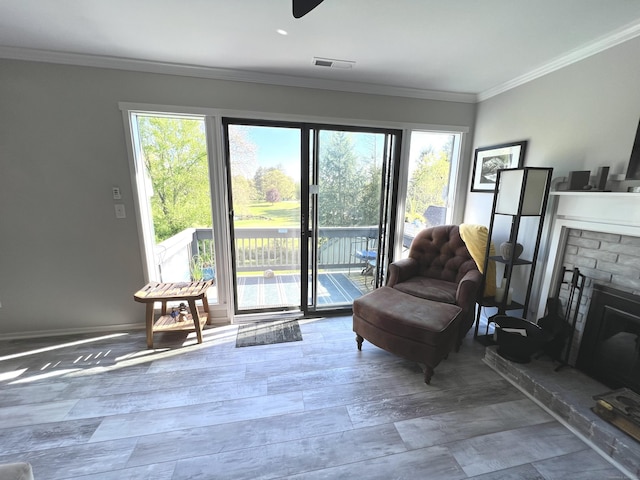sitting room with healthy amount of natural light, ornamental molding, a brick fireplace, ceiling fan, and wood finished floors