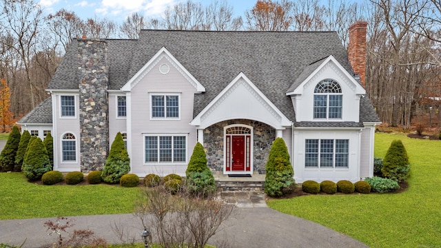 view of front of property with a front yard, stone siding, a shingled roof, and a chimney