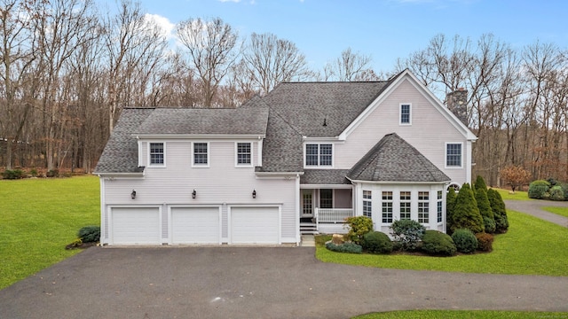 view of front of home featuring a chimney, aphalt driveway, a shingled roof, a garage, and a front lawn