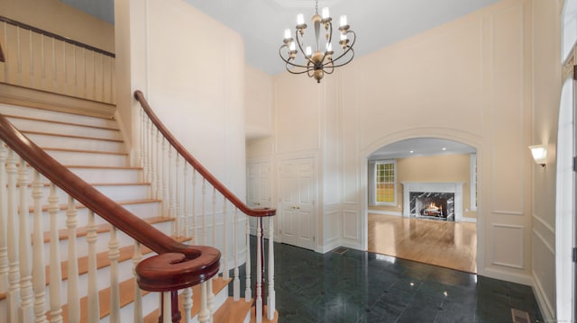 entrance foyer with a high end fireplace, dark tile patterned flooring, a high ceiling, and an inviting chandelier