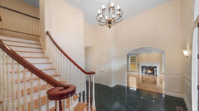entryway featuring an inviting chandelier, stairs, a decorative wall, a high end fireplace, and a towering ceiling