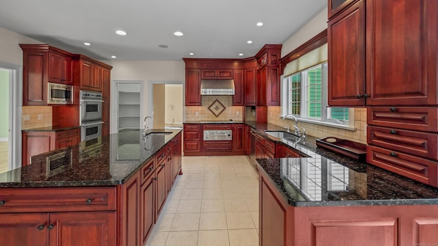 kitchen with dark stone countertops, sink, a center island with sink, and appliances with stainless steel finishes