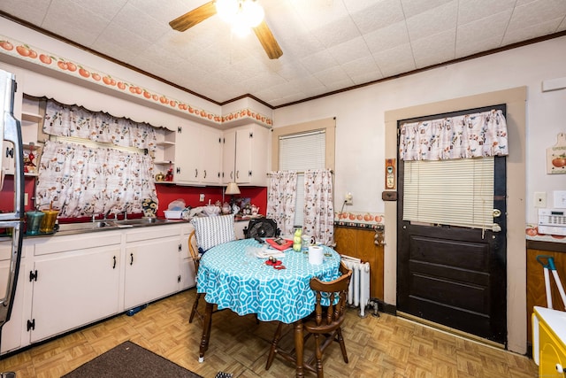 kitchen featuring ceiling fan, crown molding, white cabinets, radiator heating unit, and light parquet flooring