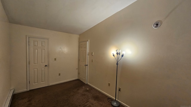 empty room featuring a baseboard radiator, dark carpet, and lofted ceiling