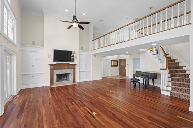 unfurnished living room featuring a high ceiling, dark hardwood / wood-style flooring, ceiling fan, and ornamental molding