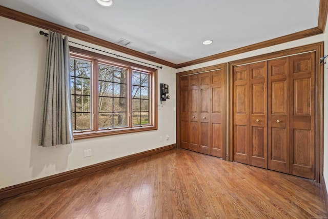 unfurnished bedroom featuring two closets, ornamental molding, and light wood-type flooring