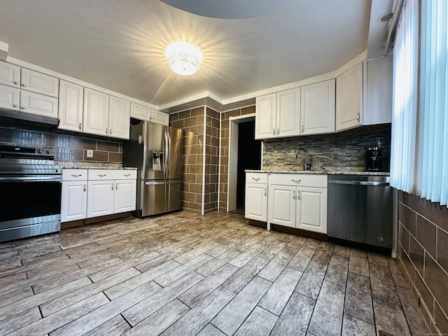 kitchen featuring white cabinetry, light stone counters, light hardwood / wood-style flooring, tile walls, and appliances with stainless steel finishes