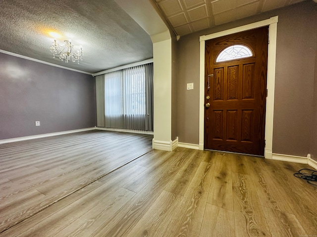 foyer entrance with a textured ceiling, a notable chandelier, crown molding, and light hardwood / wood-style flooring