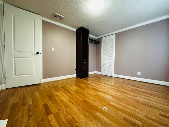 unfurnished bedroom featuring a closet, crown molding, a textured ceiling, and light hardwood / wood-style flooring