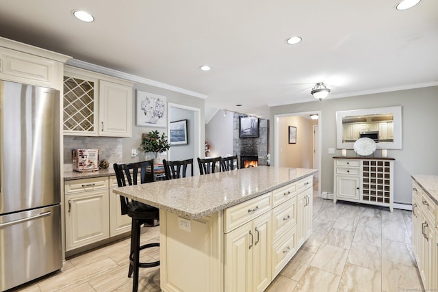 kitchen featuring a breakfast bar, stainless steel appliances, a fireplace, light stone countertops, and cream cabinetry