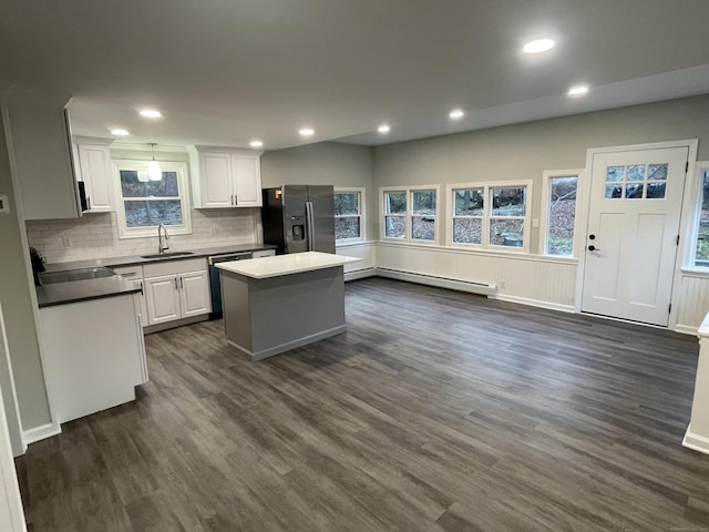 kitchen featuring white cabinets, appliances with stainless steel finishes, a kitchen island, a baseboard heating unit, and sink