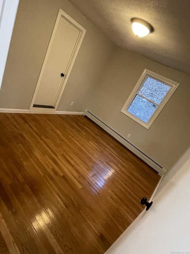 additional living space featuring a textured ceiling, wood-type flooring, and a baseboard radiator