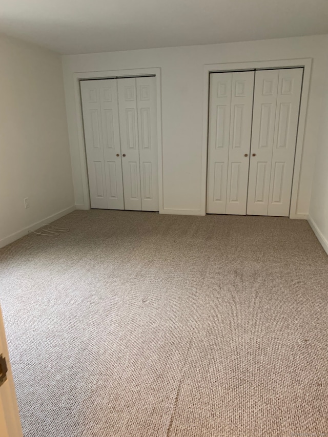 unfurnished bedroom featuring carpet flooring and multiple closets