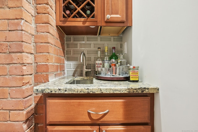 bar featuring light stone counters, sink, and brick wall