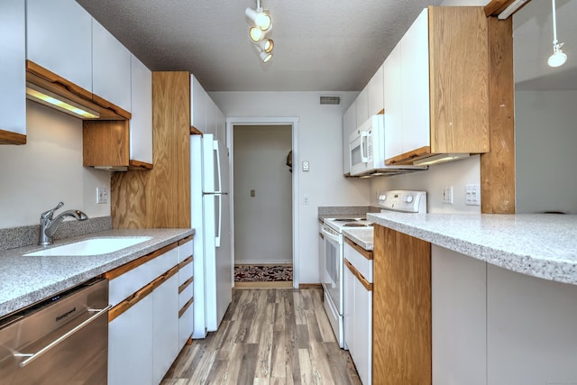 kitchen with white appliances, sink, light wood-type flooring, decorative light fixtures, and white cabinetry